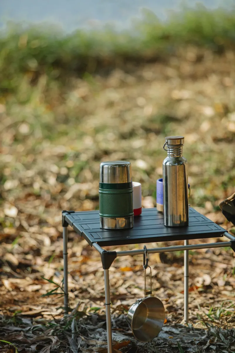 Portable camping table with flasks beside the water