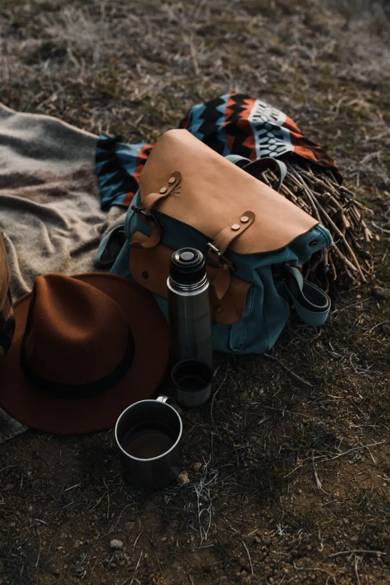 Backpack, flask and hat arranged on a picnic blanket