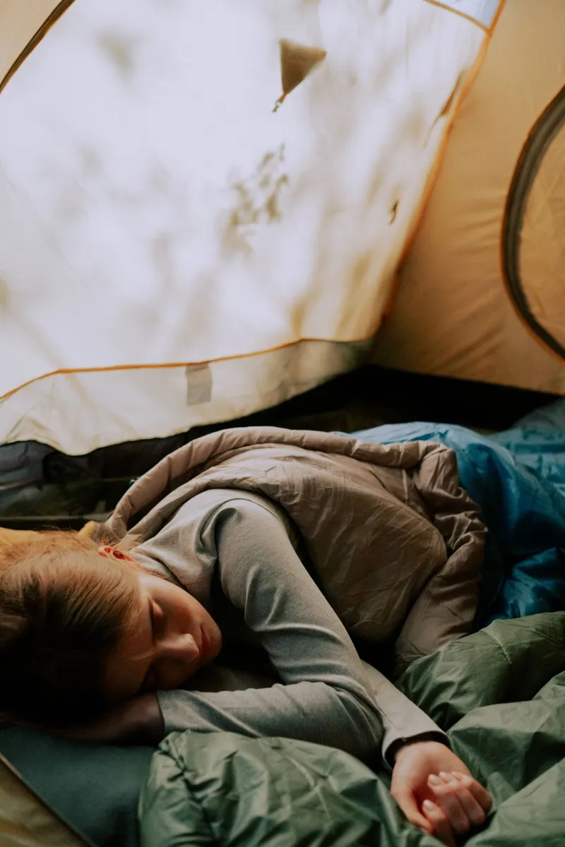 Camper resting in a sleeping bag inside a tent
